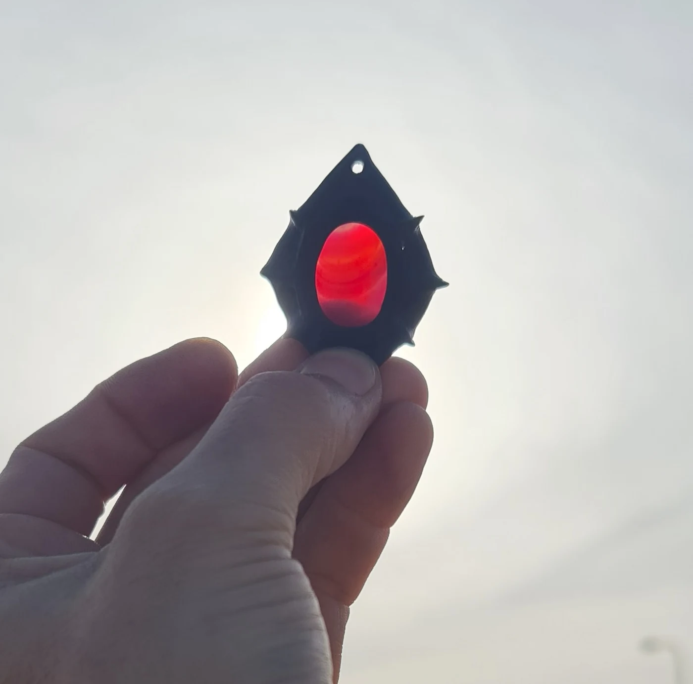 Sol de Ébano, amuleto de ébano y piedra magenta sostenido frente al sol